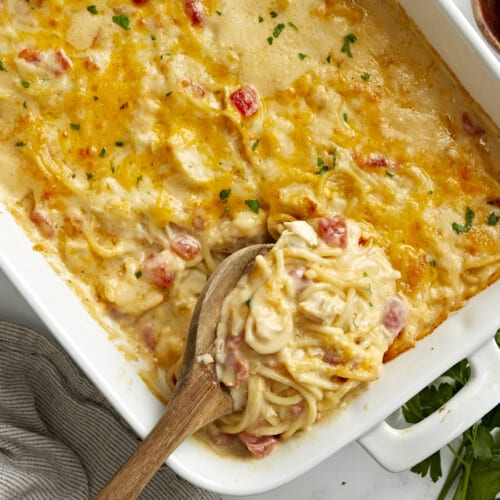 Overhead view of chicken spaghetti in a white casserole dish with a wooden spoon placed inside.