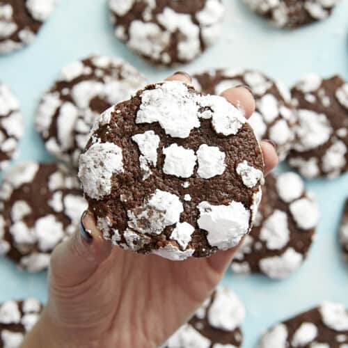 A hand holding a chocolate crinkle cookie close to the camera with others in the background