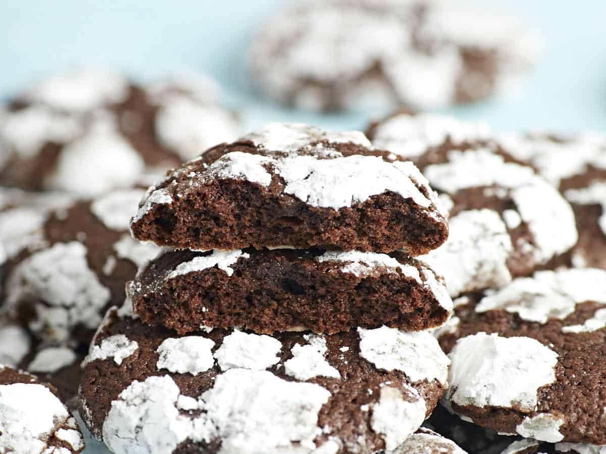 A stack of chocolate crinkle cookies with the one on top broken in half exposing the inside.