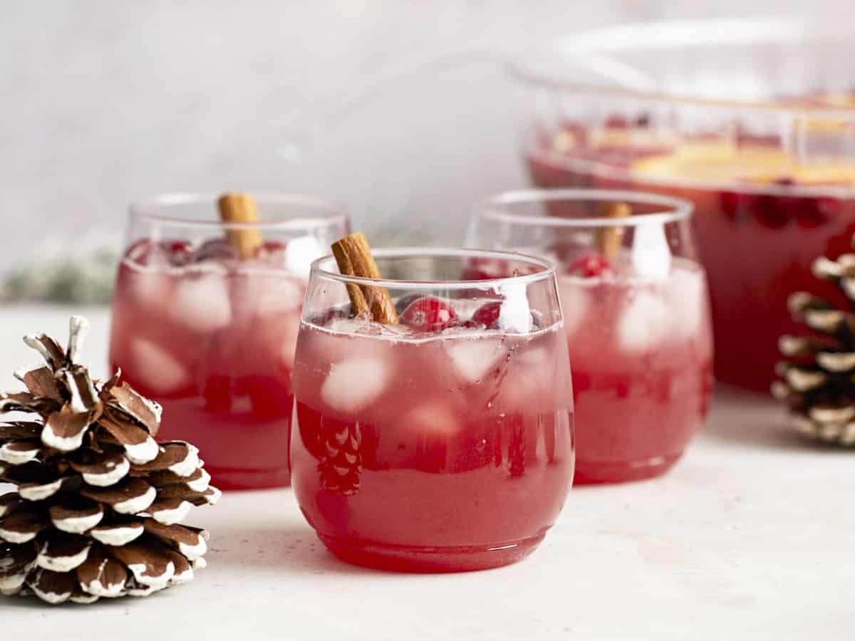 Side view of three glasses of Christmas Punch garnished with cinnamon with the punch bowl in the back. 