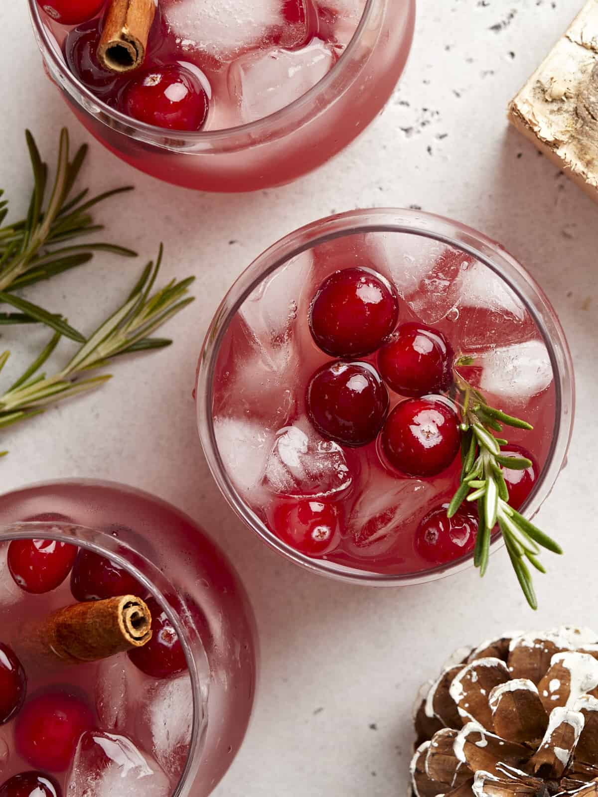 Overhead view of three glasses of Christmas punch garnished with cranberries and fresh rosemary.