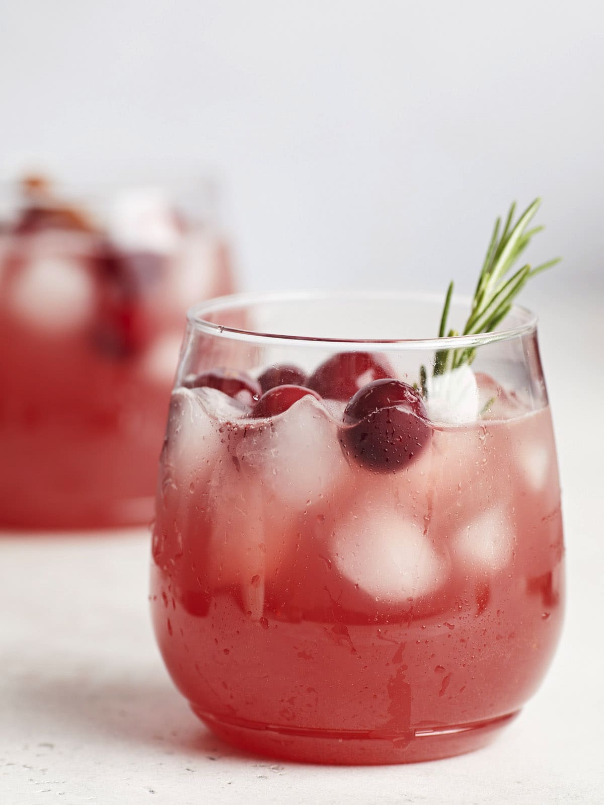 Close up side view of two glasses of Christmas punch garnished with cranberries and fresh rosemary. 