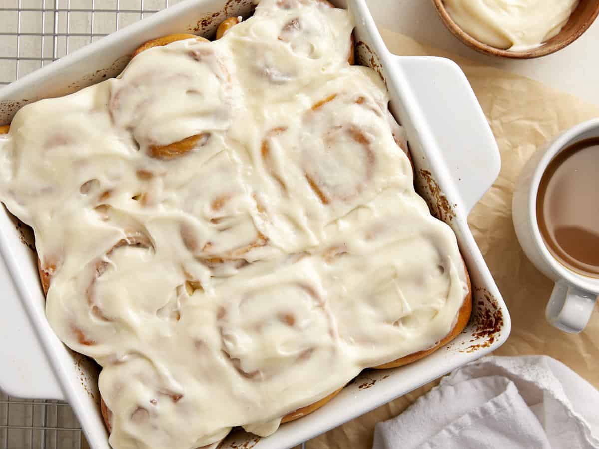 Overhead view of frosted cinnamon rolls in a baking dish with coffee on the side. 