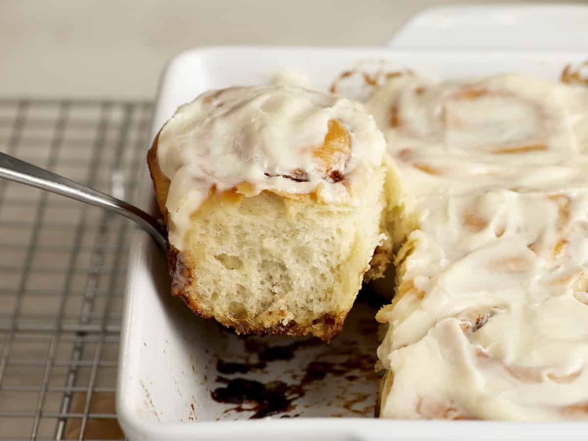 Side view of a cinnamon roll being lifted out of the baking dish.