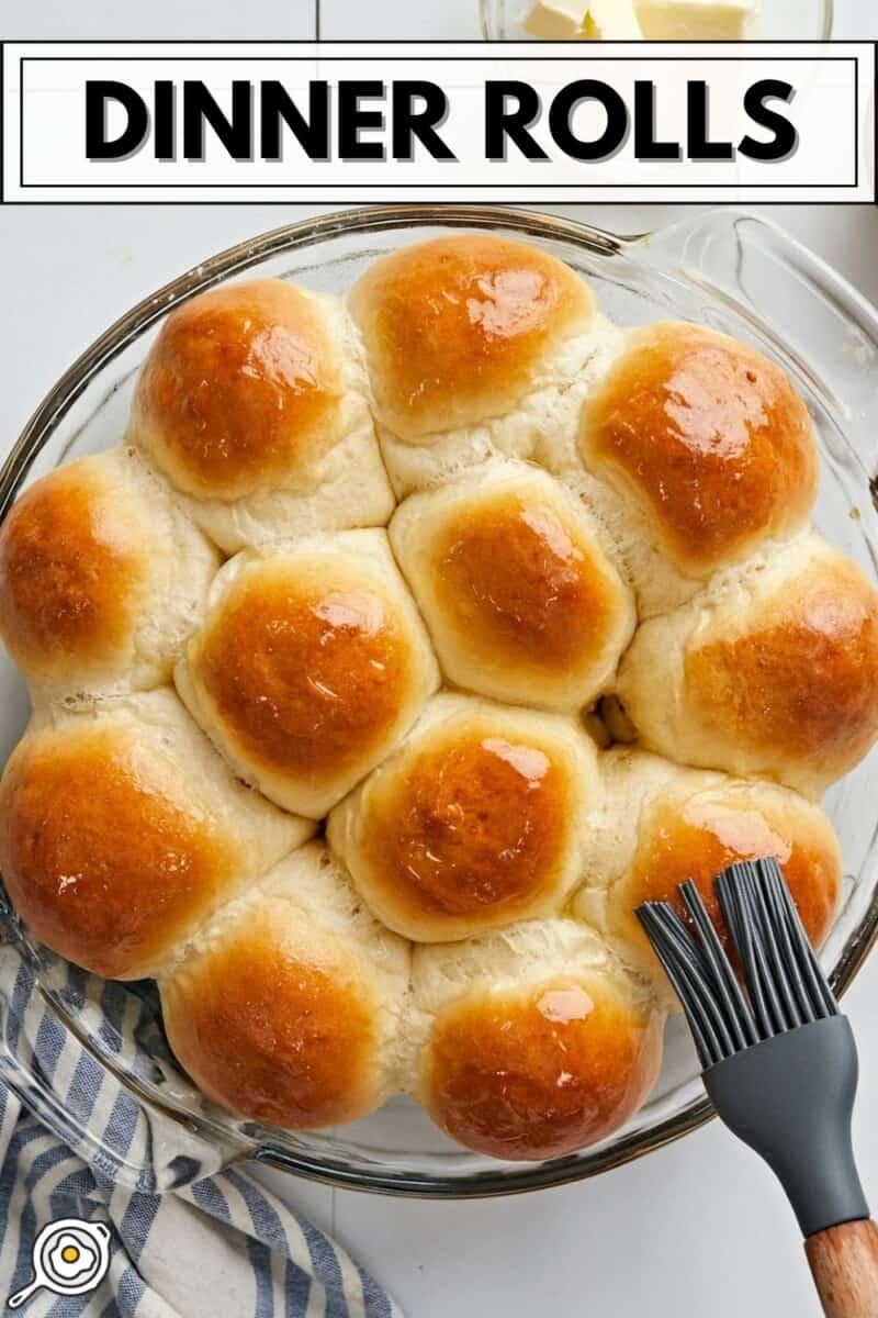 Overhead view of dinner rolls in a round baking dish being brushed with butter.