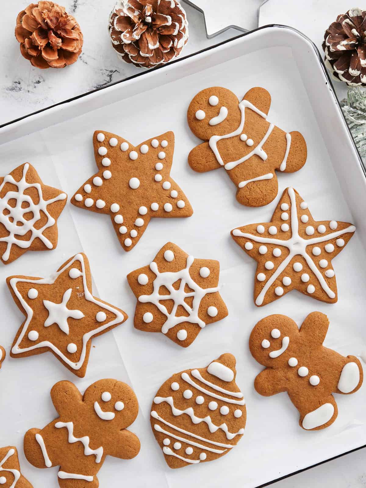Decorated gingerbread cookies on a baking sheet surrounded by pinecones.