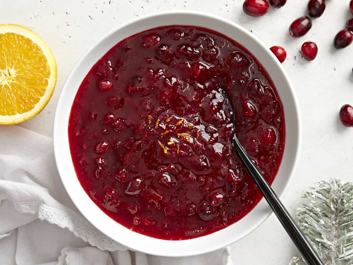 Overhead view of cranberry sauce in a bowl with orange zest and a spoon. 