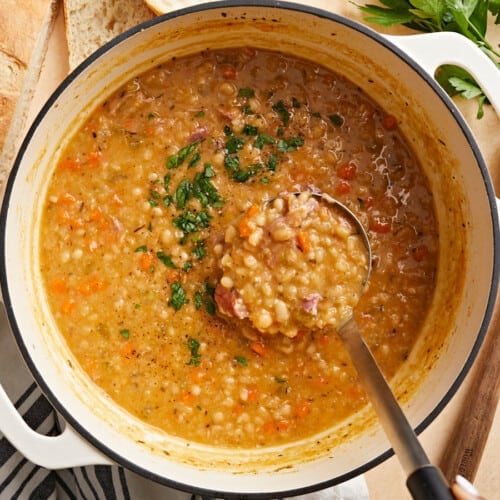 Overhead view of a dutch oven pot full of navy bean soup with a ladle scooping some out.