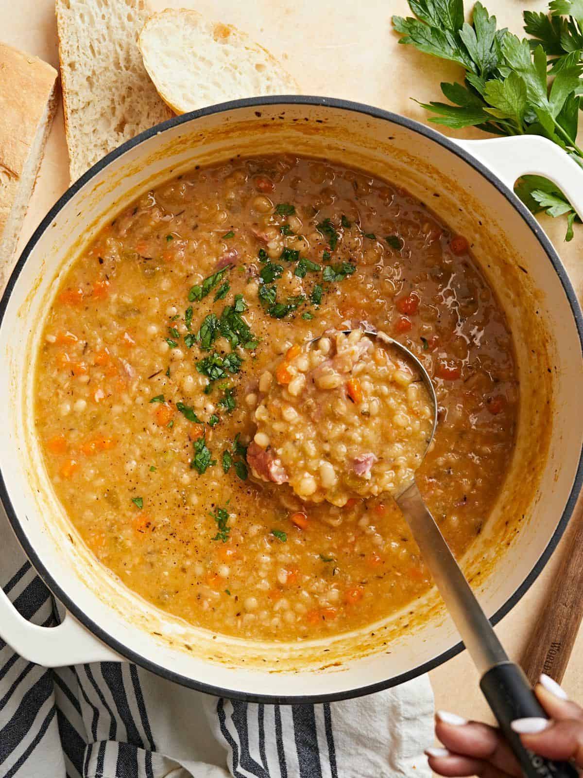 Overhead view of a pot of Navy Bean Soup with a ladle scooping some out.