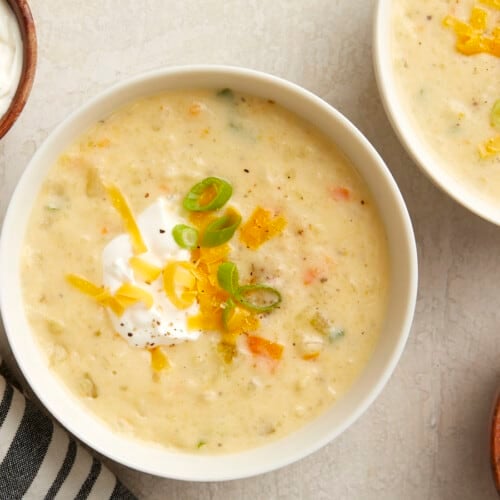 Overhead photo of slow cooker potato soup in a white bowl with sour cream, green onions, and shredded cheese on top.