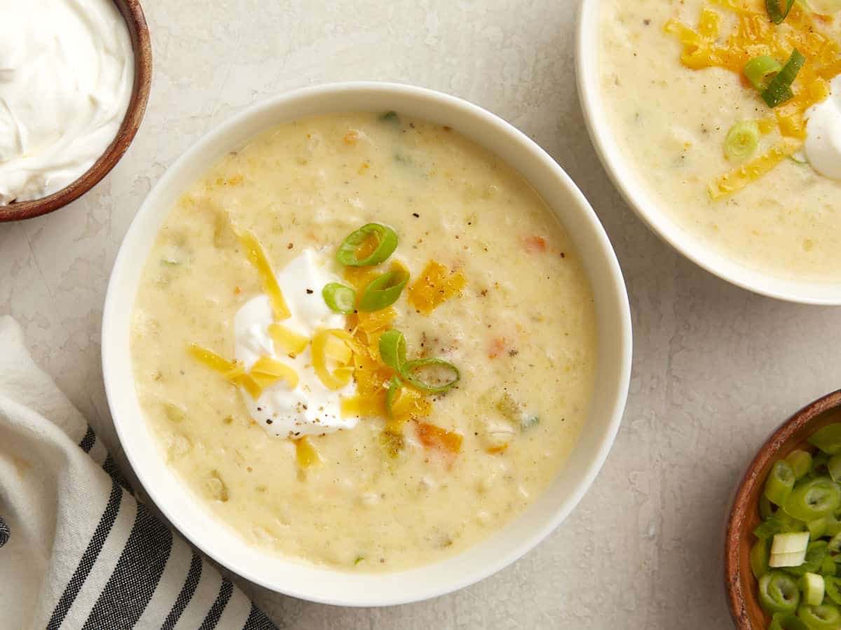 Overhead photo of slow cooker potato soup in a white bowl with sour cream, green onions, and shredded cheese on top.