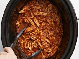 Close overhead view of salsa chicken in the crock pot with tongs.