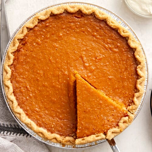 Overhead view of a whole sweet potato pie with one slice cut and being lifted out of the pie pan.