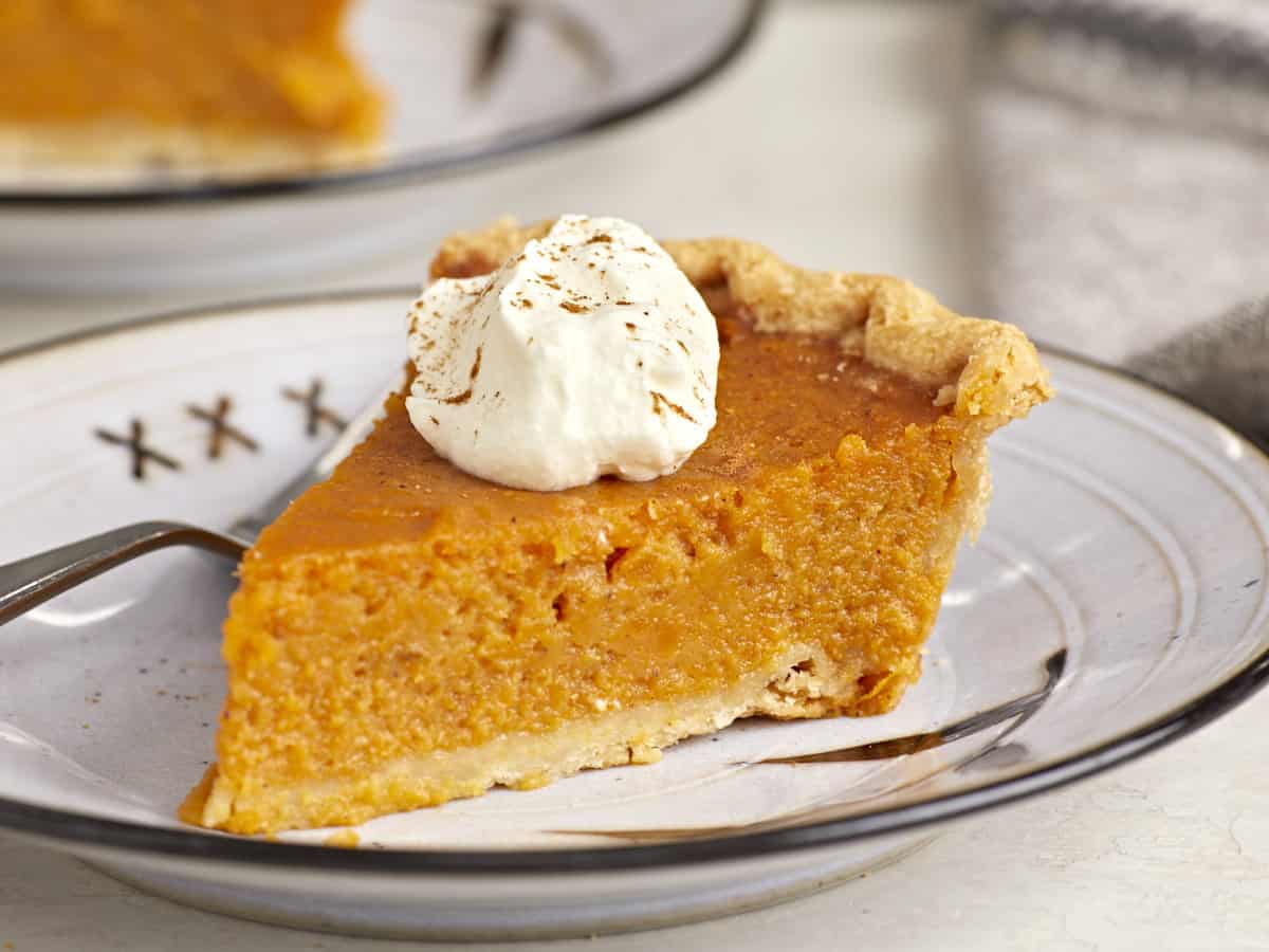 Side view of a slice of sweet potato pie on a plate with whipped cream on top.