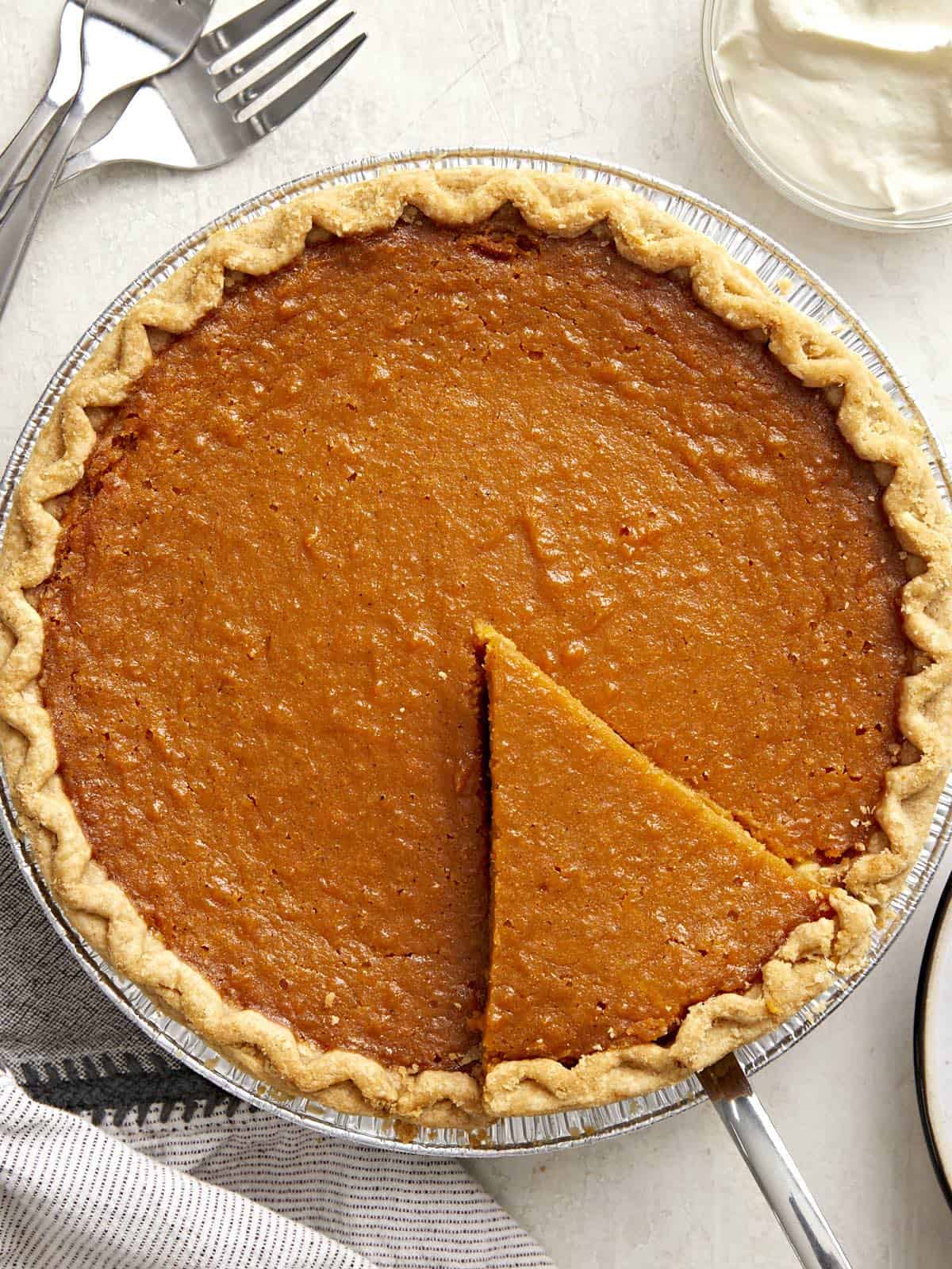 Overhead view of a whole sweet potato pie with one slice cut and being lifted out of the pie pan.