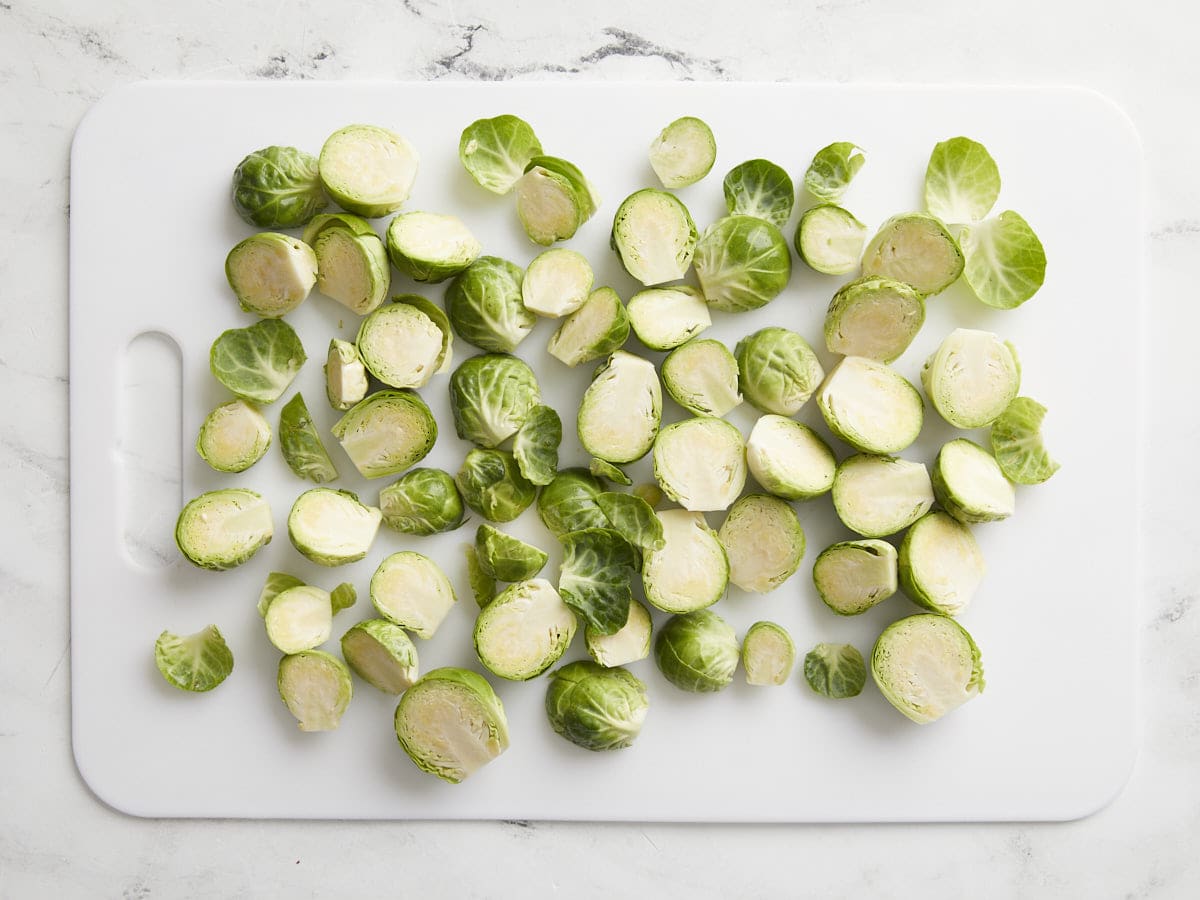 Brussel sprouts sliced in half on a white cutting board.