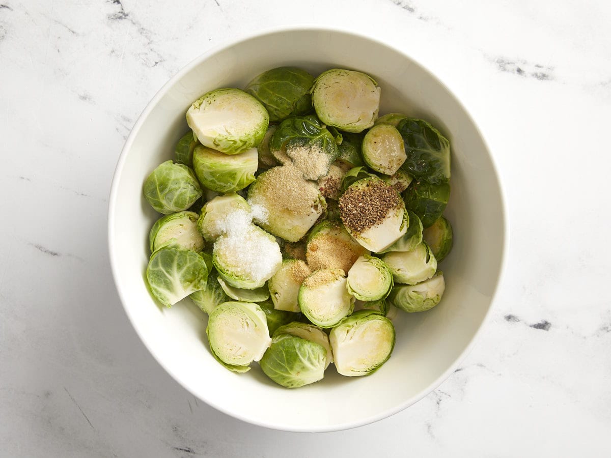 Halved Brussels sprouts in a bowl with olive oil and spices.