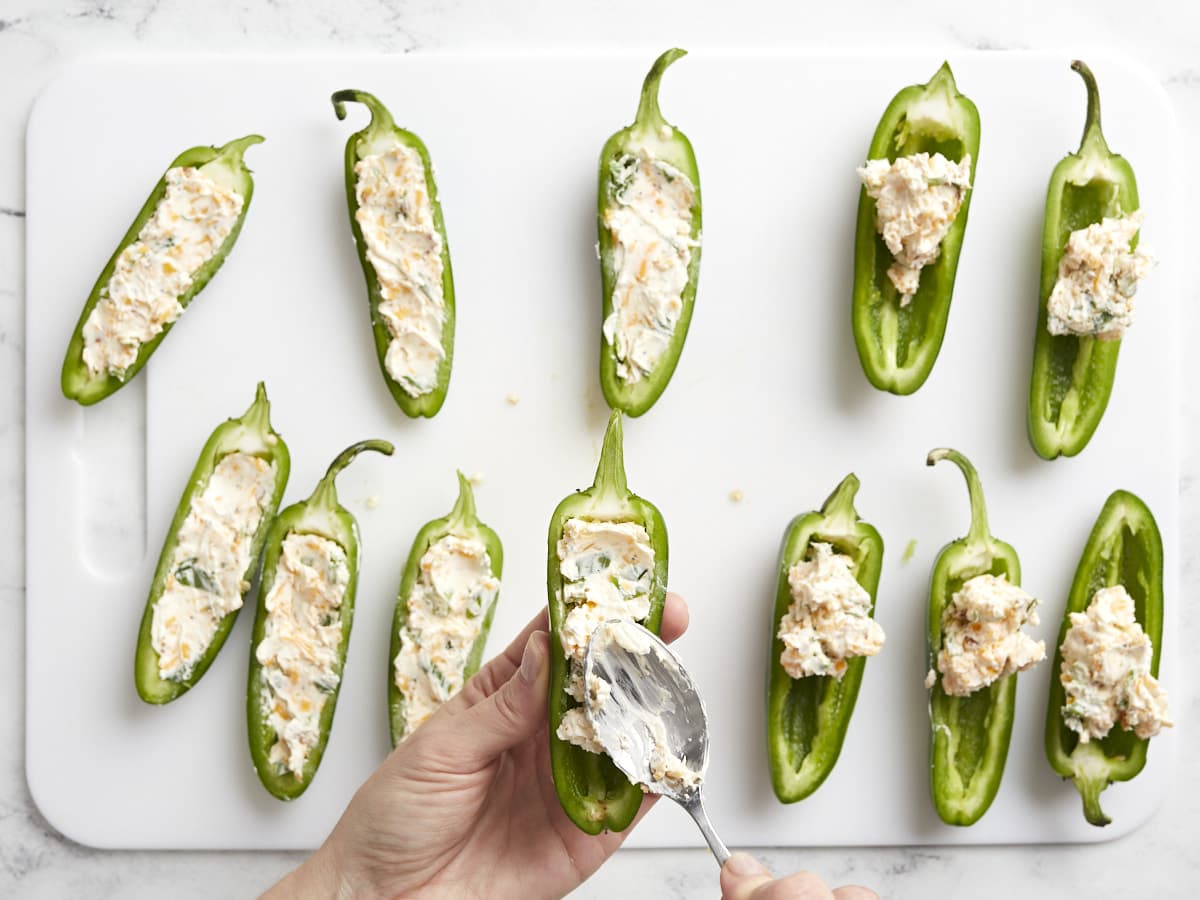 Cheese filling being spooned into jalapeño halves. 