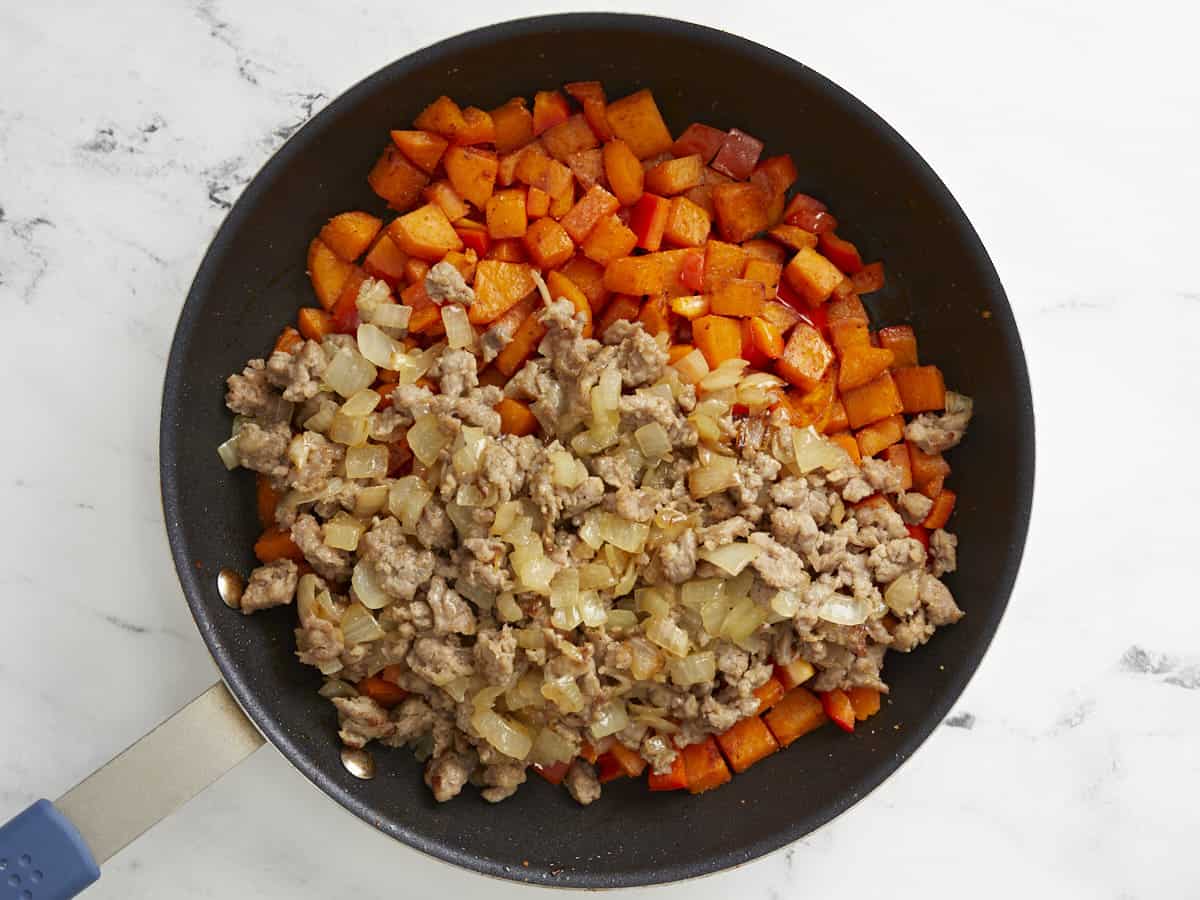 Ground sausage and onion added to cooked sweet potatoes in a skillet.