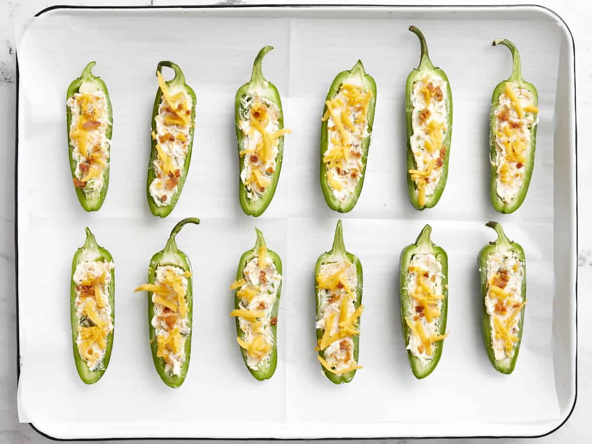Jalapeño poppers ready to bake on a parchment-lined sheet pan. 