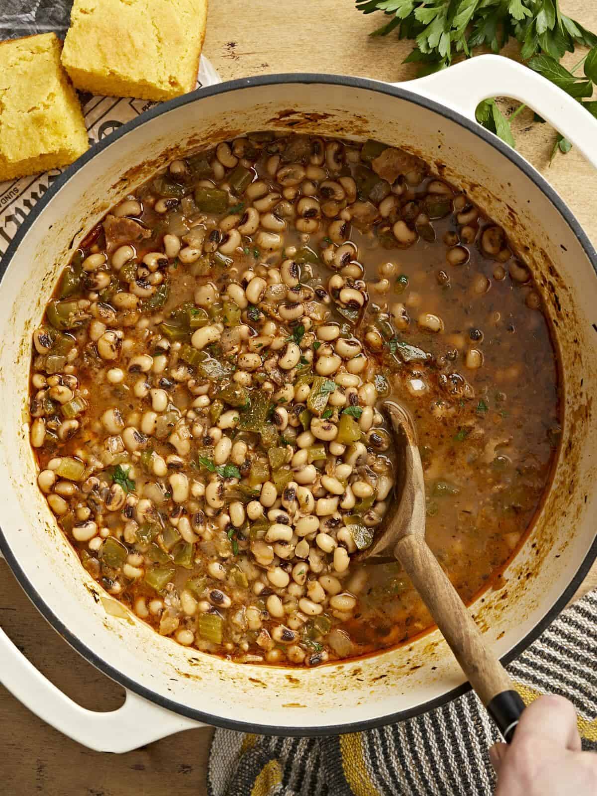 Overhead view of a pot of black-eyed peas being stirred with a wooden spoon.