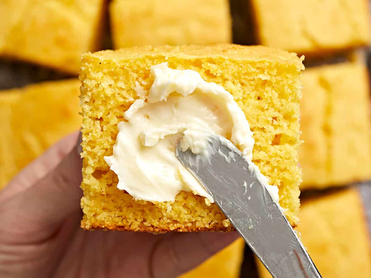 Close up of butter being spread onto a piece of cornbread. 