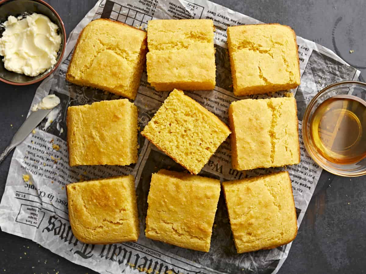 Squares of cornbread on parchment with honey and butter on the sides.