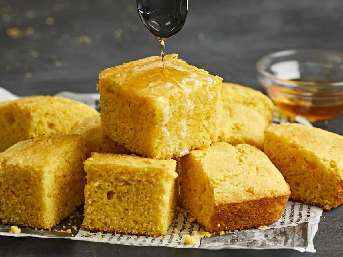 A stack of cornbread squares with honey being drizzled over top.