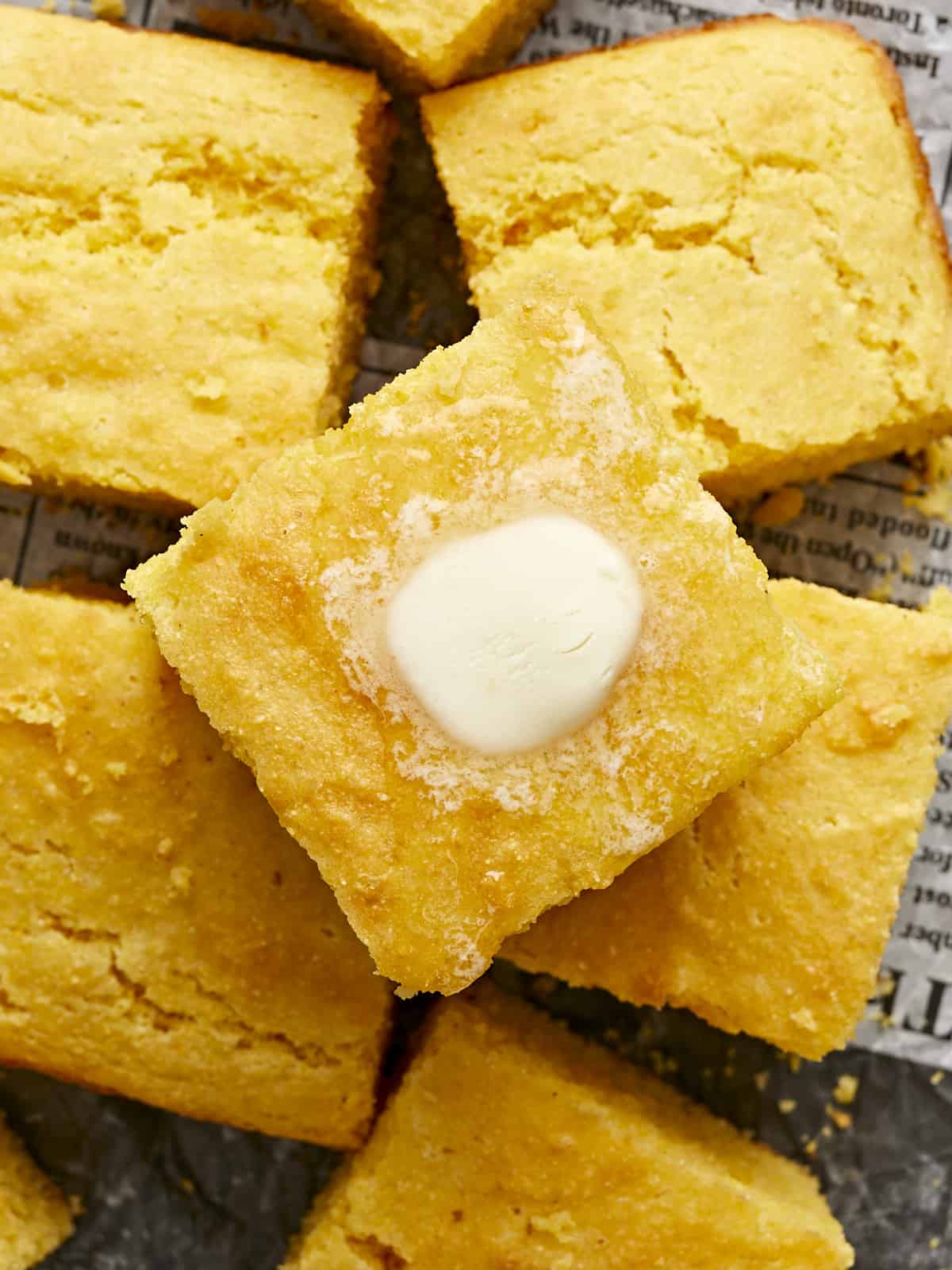 Close up overhead view of a stack of cornbread squares with melting butter on top.