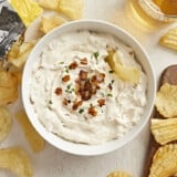Overhead view of a trencher of French Onion Dip with a tweedle in the side and fries all around.