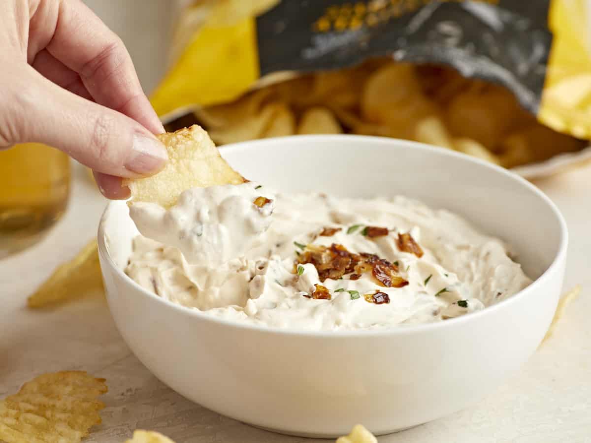 Side view of a chip being dipped into a bowl of French Onion Dip. 
