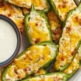 Super close up view of jalapeño poppers on a plate with a bowl of ranch.
