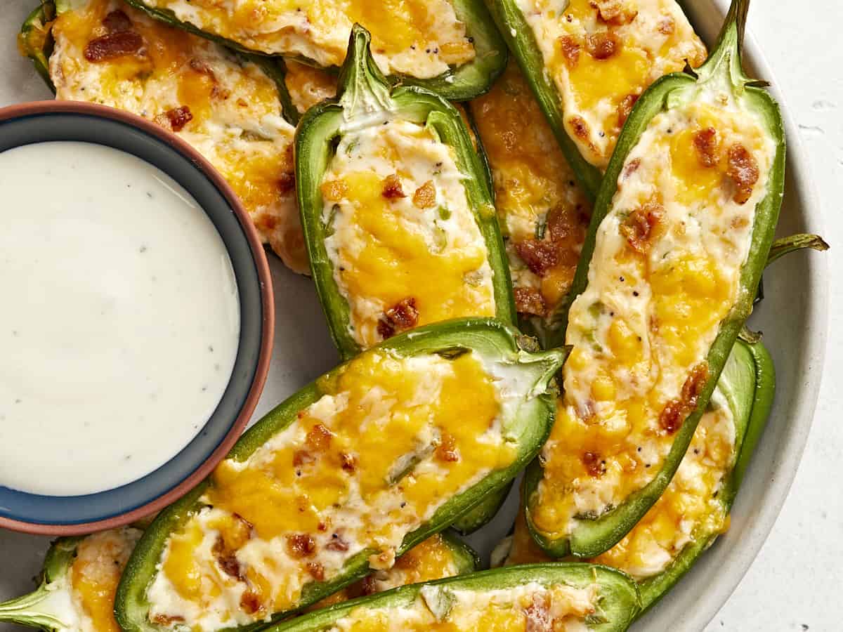 Super close up view of jalapeño poppers on a plate with a bowl of ranch. 