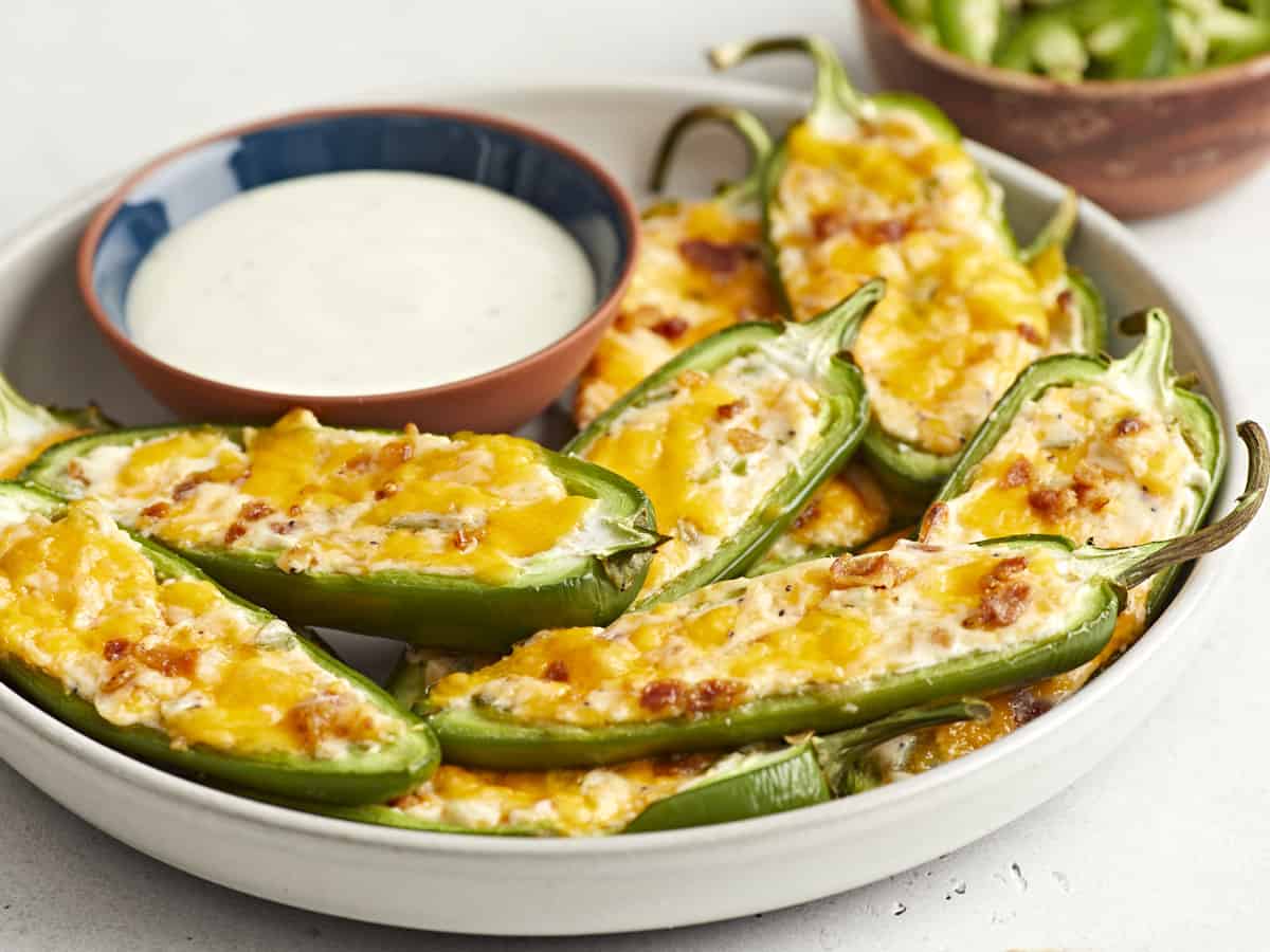 Side view of a plate full of jalapeño poppers with a dish of ranch on the side. 