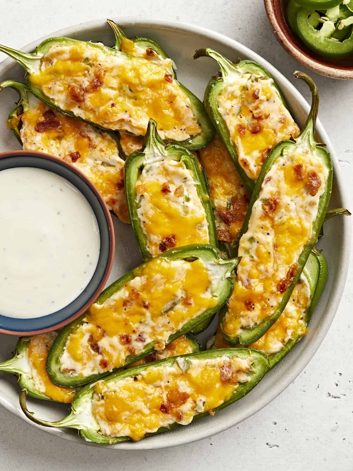 Overhead view of a plate full of jalapeño poppers with a dish of ranch dressing.