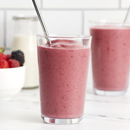 Front view of two mixed berry smoothies in a glass with a metal straw.