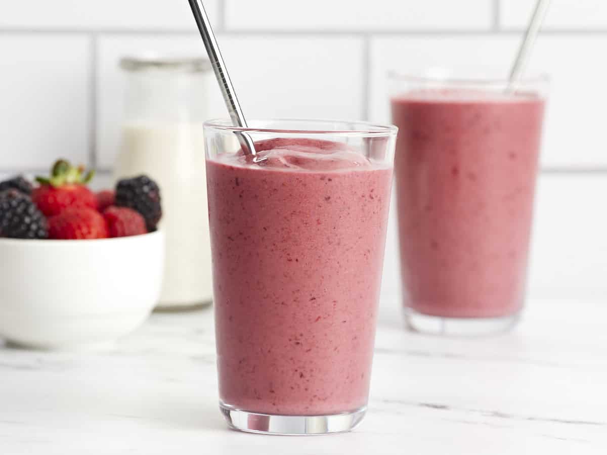 Front view of two mixed berry smoothies in a glass with a metal straw.