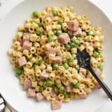 Overhead view of a bowl full of pasta with peas and ham and a fork.