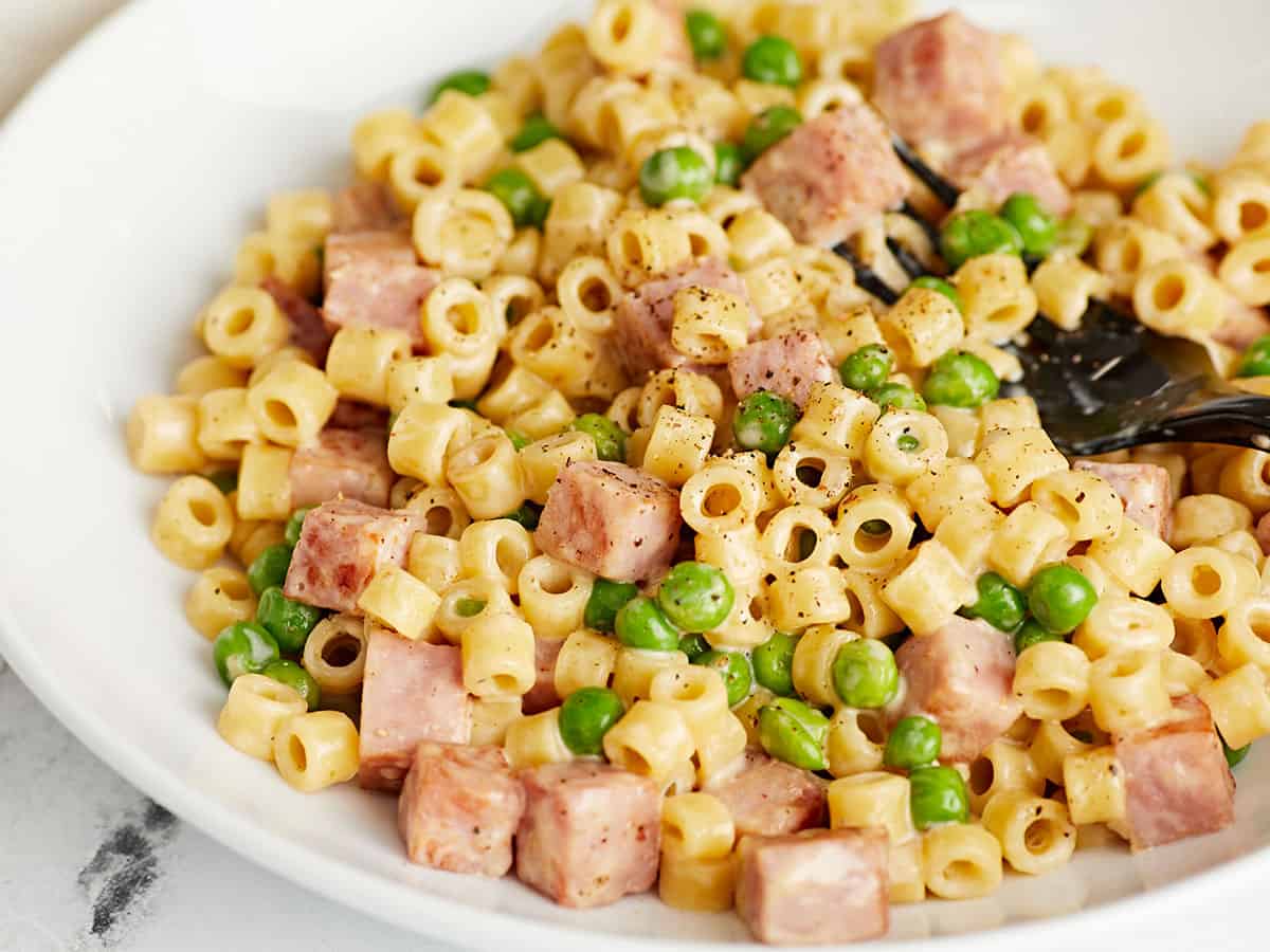 Close up side view of a bowl of pasta with peas and ham. 