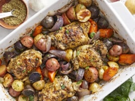 Overhead view of roasted chicken and vegetables in a white casserole dish.