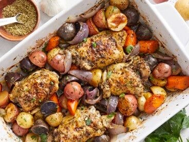 Overhead view of roasted chicken and vegetables in a white casserole dish.