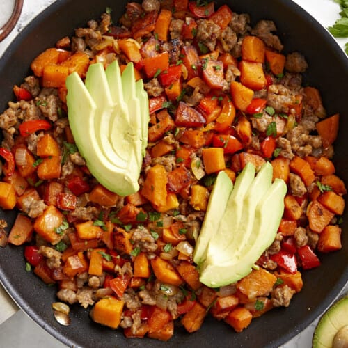 Overhead view of sweet potato hash in a skillet garnished with sliced avocado.