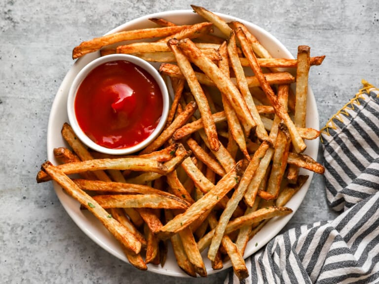Overhead view of air fryer french fries on a white plate with ketchup.