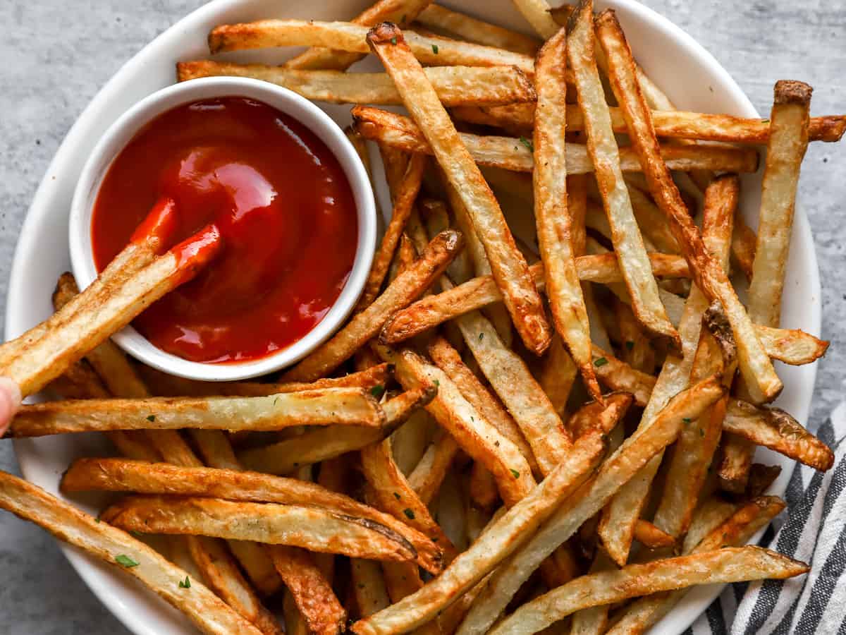 Overhead view of 2 french fries dipped into ketchup on a platter of fries.