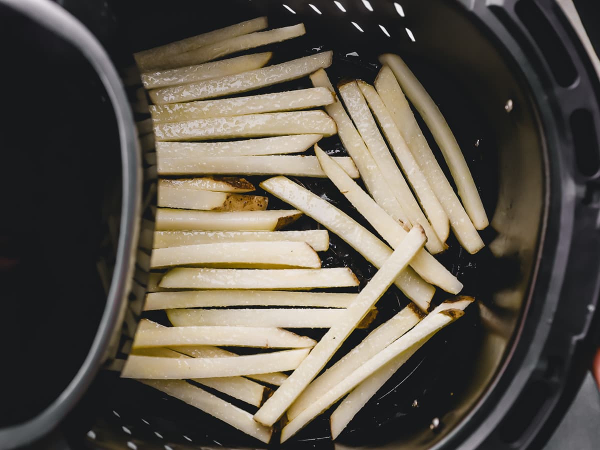 raw french fries in the basket of an air fryer.