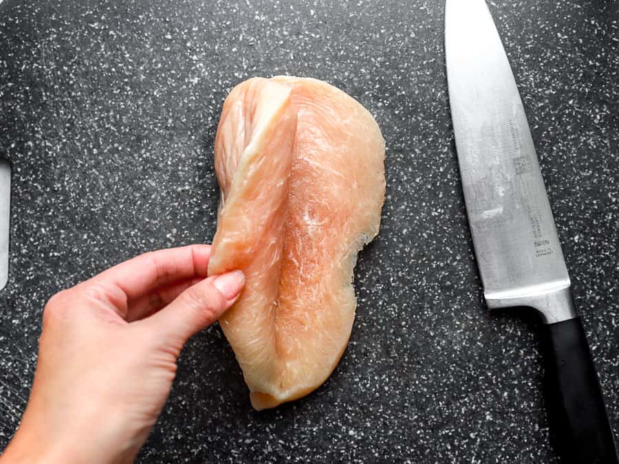 a hand opening a butterflied chicken breast next to a knife.
