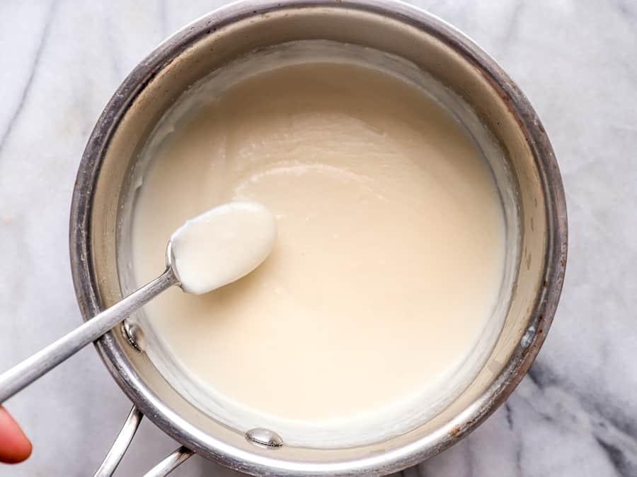 thick and creamy white sauce in a saucepan with a spoon.
