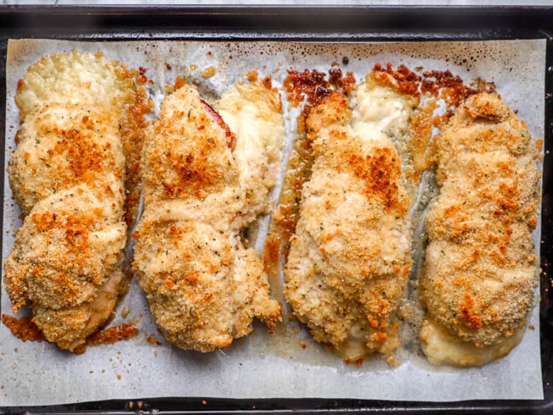 4 breaded and baked rolled-up chicken breasts on a baking sheet.