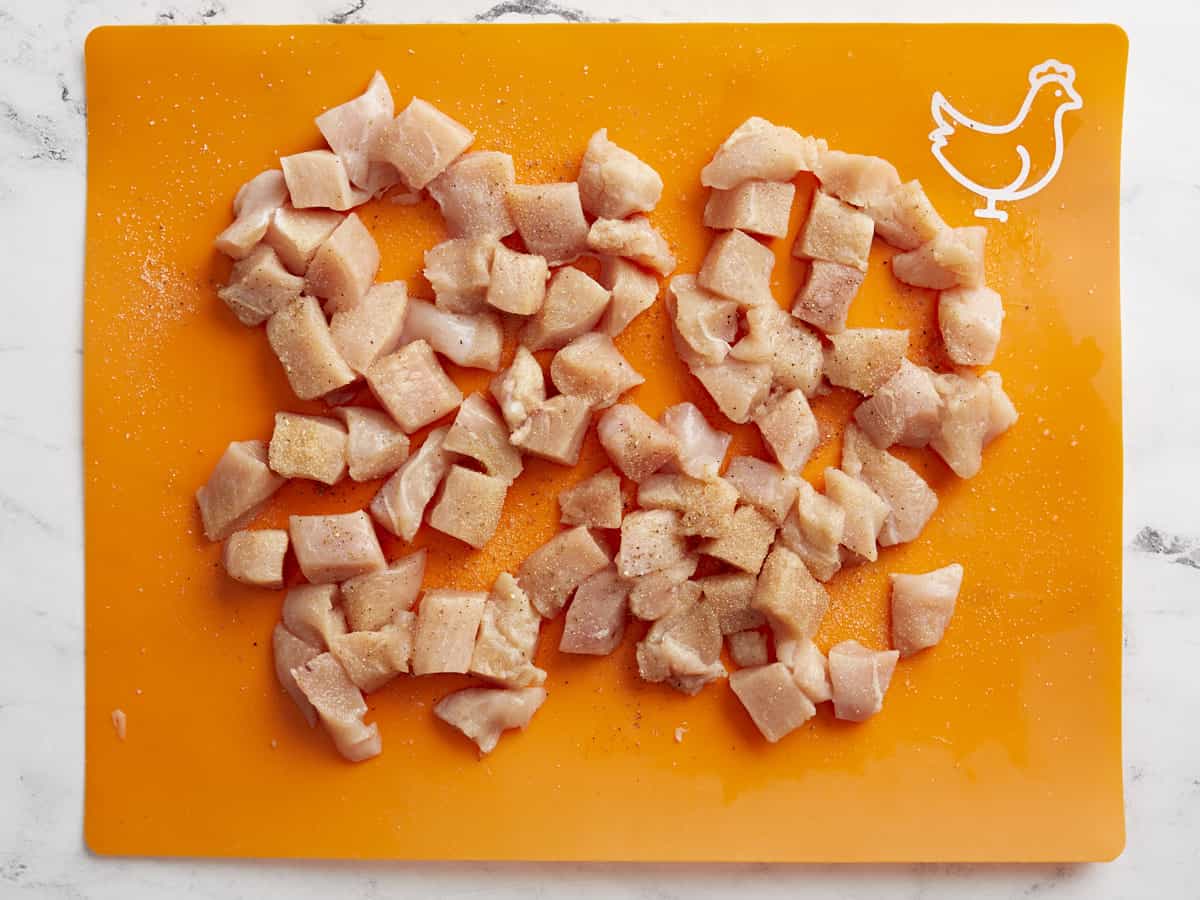 Chicken breasts cut into bite size pieces on a cutting board.