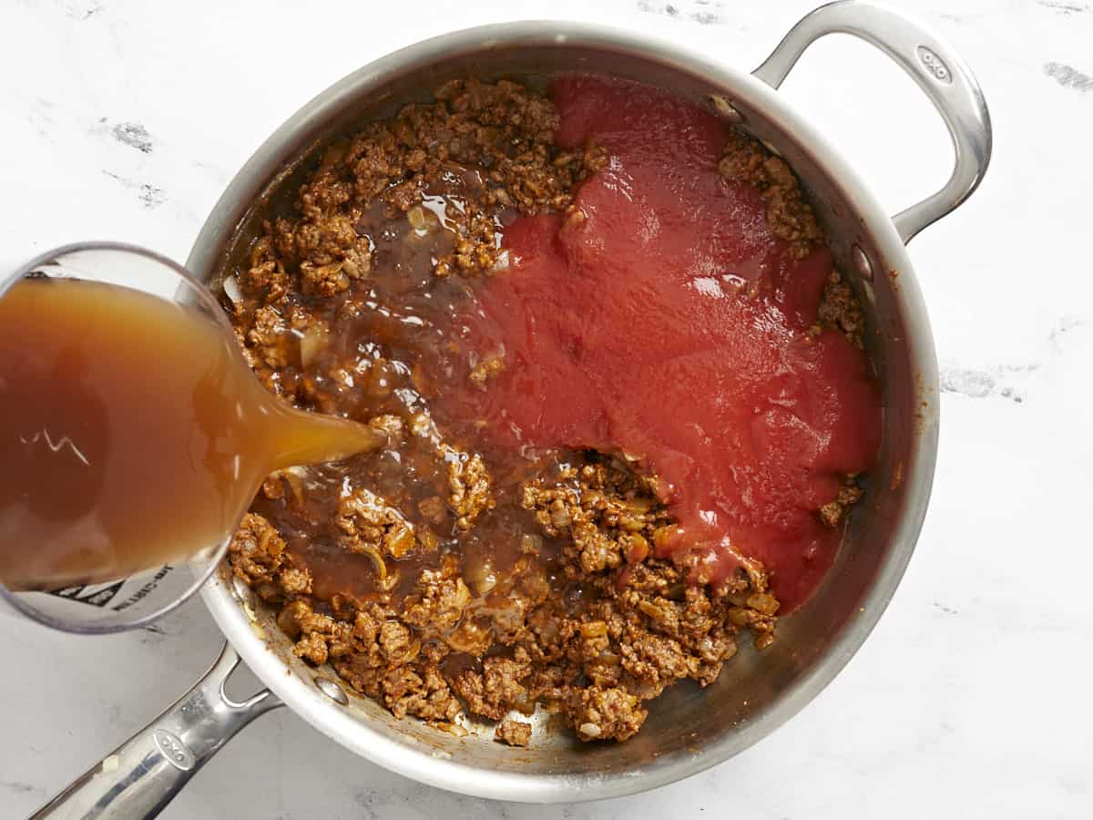 Tomato sauce added to the skillet and beef broth being poured into the side. 